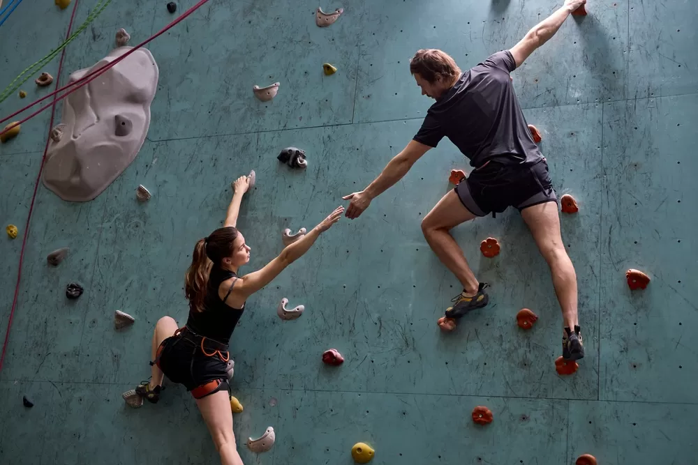 A man helping a woman up on an indoor rock climbing course.