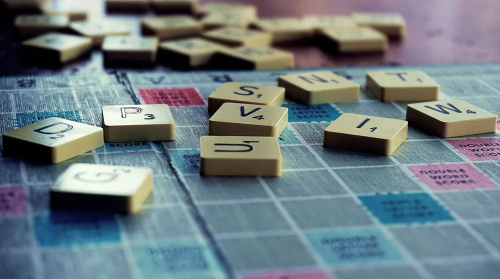 Closeup of a scrabble board game with tiles randomly strewn across the board.