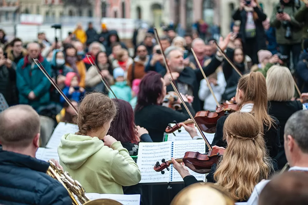 A group of people playing music in the street with violins and a conductor.