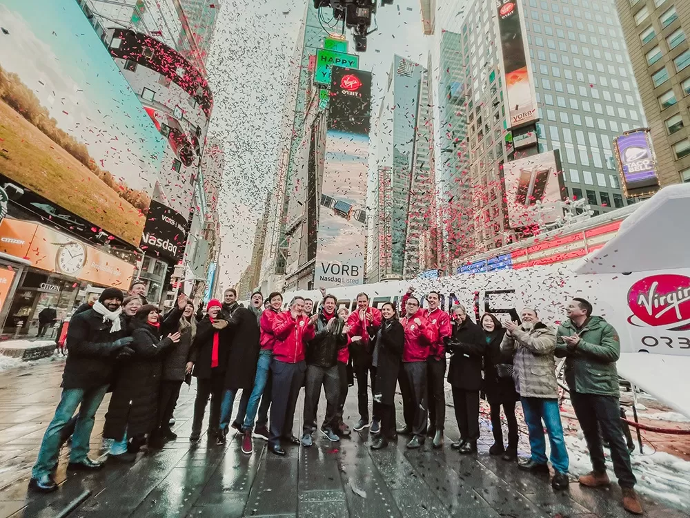 A group of Virgin employees standing in times square clapping while confetti falls from the sky.