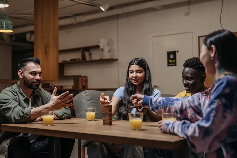 A group of people sitting at a table playing Jenga and drinking orange juice.