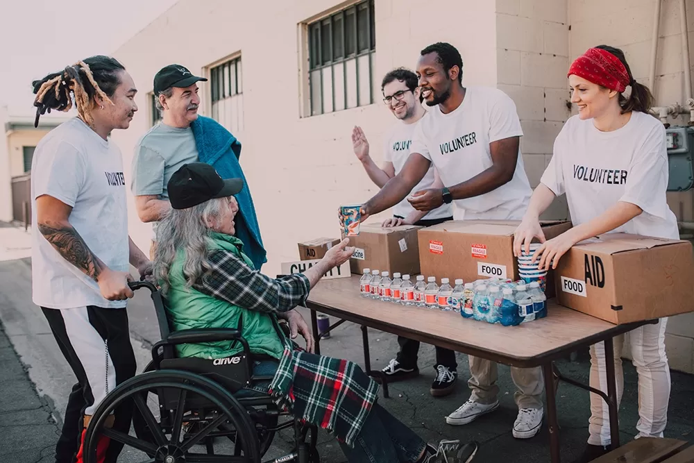 A table with people handing out drinks to another group of people with one in a wheel chair.