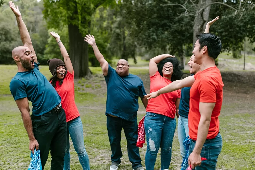 A group of excited people wearing different colored shirts holding their hands in the air and laughing.