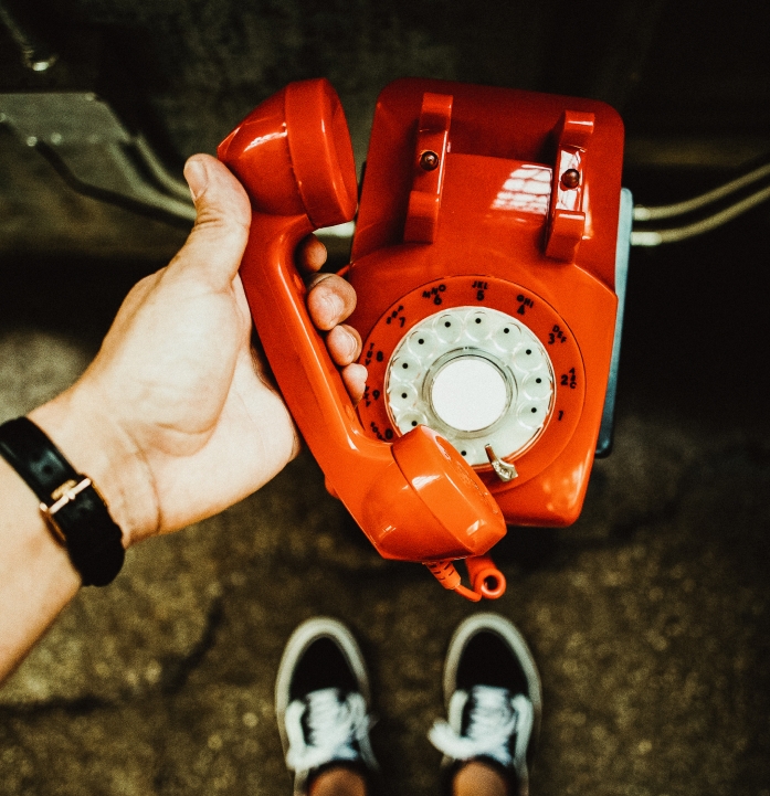A hand holding a red landline rotary phone.