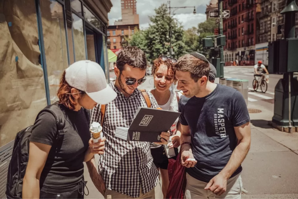 A group of people standing in the street in New York City looking at a puzzle box together.