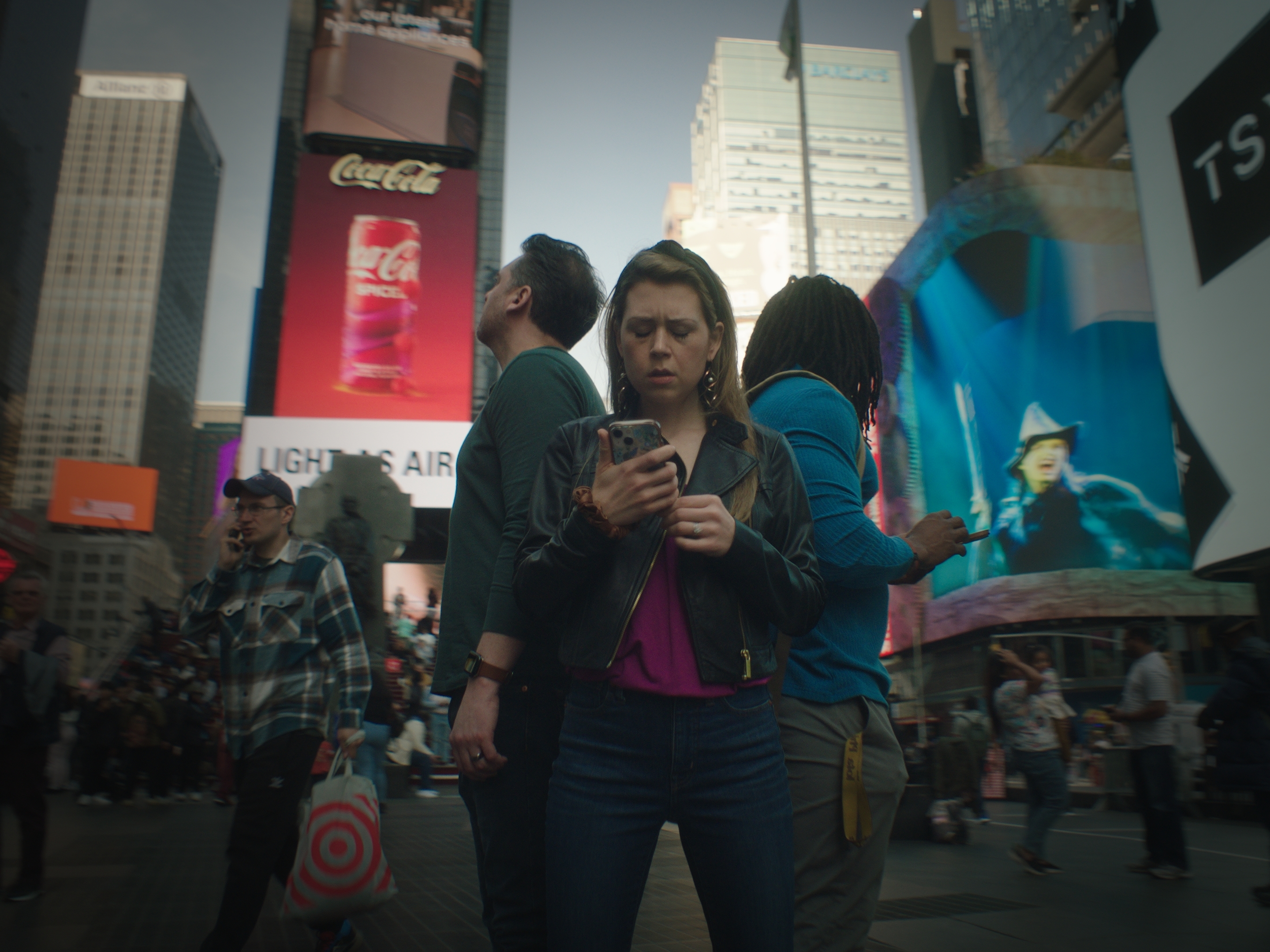 Three people stand back to back in times square looking at a cellphone and the billboards around.