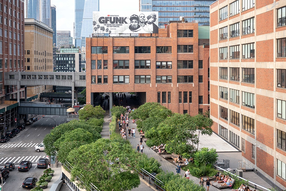 Aerial view of the high line by Chelsea Market. A walking path on the second story, with lots of trees and nice buildings surrounding it.