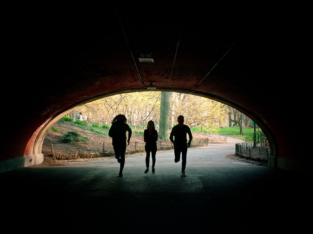 Three people running in the shadows through a tunnel.