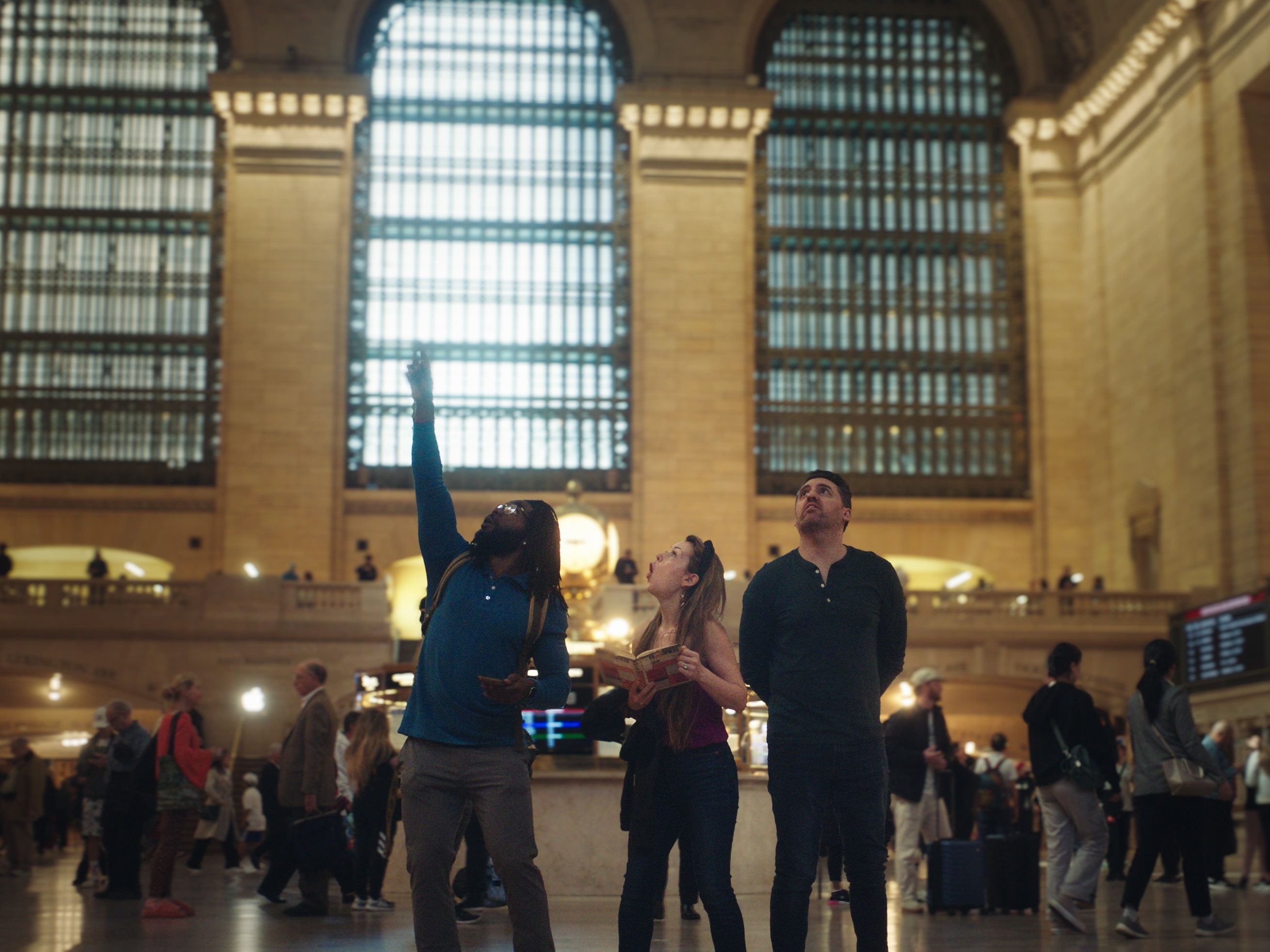 Three people in Grand Central Terminal looking at the ceiling.